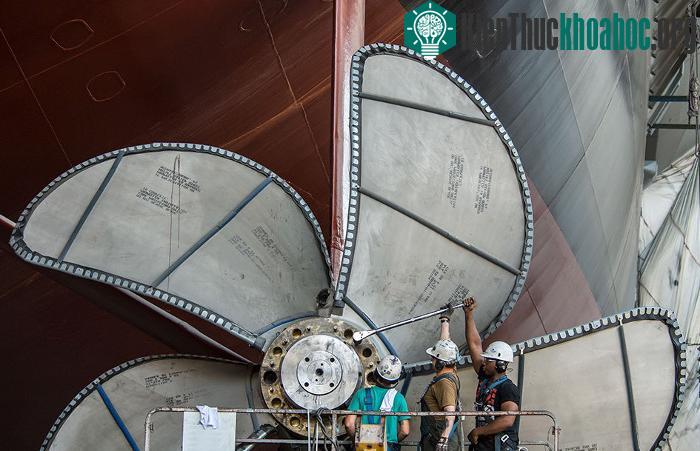 Các công nhân đang siết những con ốc trên một chân vịt của tàu USS Gerald R. Ford bằng một chiếc cần siết lực.