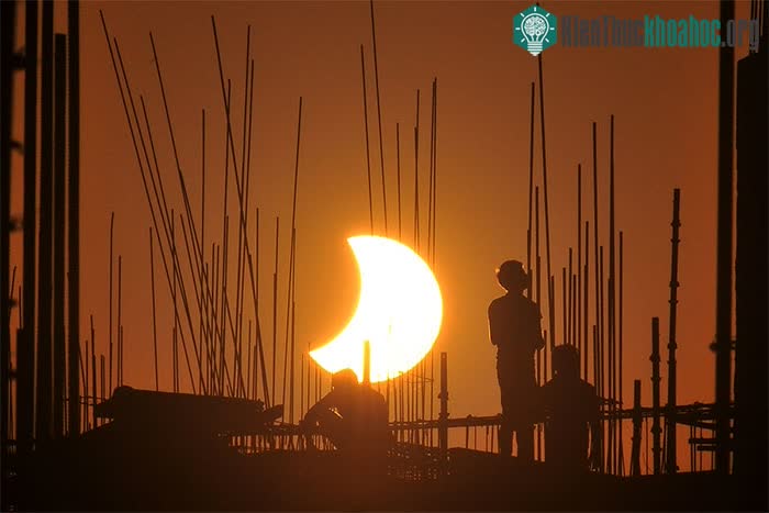ình bóng của những người lao động làm việc hiện lên nổi bật phía trước nhật thực một phần.