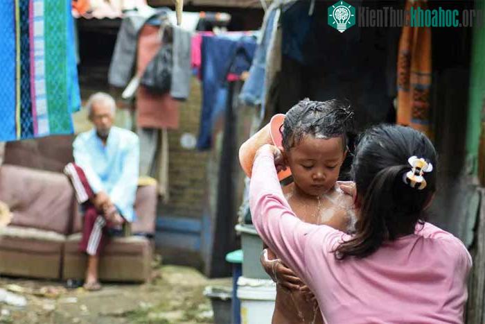 Một cô gái đang tắm cho em bằng nước từ dòng sông bị ô nhiễm rác thải sinh hoạt