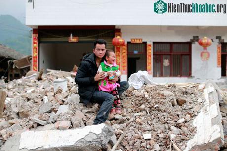 Một người đàn ông và một đứa trẻ ngồi trên đống đổ nát