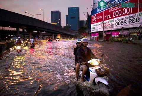Hai người dân lái xe máy trên một con đường bị ngập nặng ở quận Lat Phrao, Bangkok. (Ảnh: AFP)