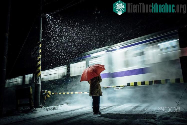 Một khách bộ hành đứng chờ tàu chạy qua trước thanh chắn barrier.