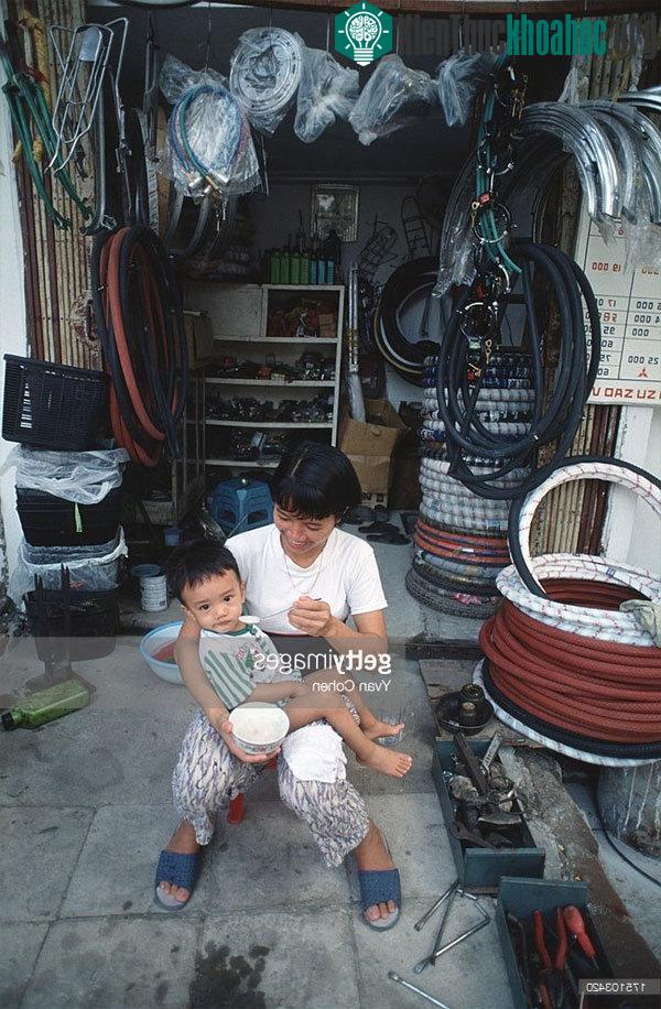 Người phụ nữ bón cho con ăn bên ngoài một cửa hàng phụ tùng xe đạp.