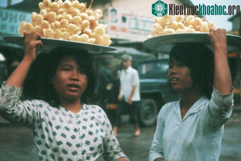 Hai cô bé đang đội mâm mía trên đầu đi bán.