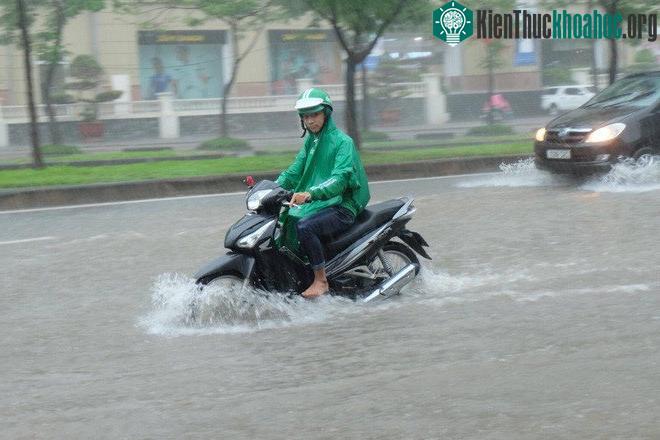 Một tài xế GrabBike đi chân không lái xe qua đoạn đường ngập sâu.