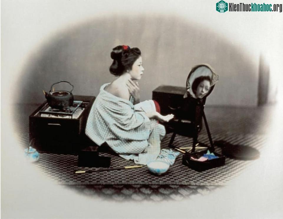 Một phụ nữ đang tô phấn trắng lên khuôn mặt và để lộ một bên vai trần.