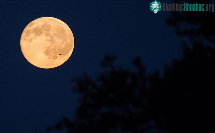 Một chiếc máy bay đang bay ngang qua phía trước Mặt Trăng trên bầu trời từ văn phòng của NASA ở Fort Myer Heights, Arlington, Virginia.