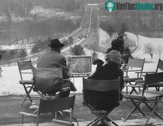 Một cặp vợ chồng theo dõi trận đấu bóng chày từ chiếc TV đặt bên ngoài một khách sạn nhỏ.