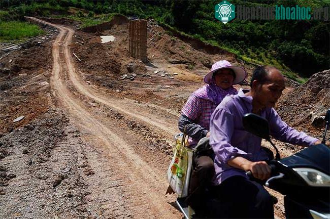Người dân chạy xe trên một con đập bị vỡ do mưa lớn tại huyện Dương Sóc ngày 16/7.