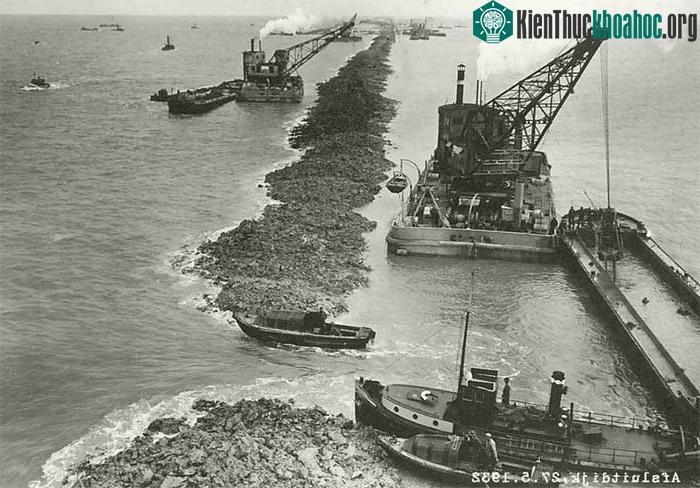 Tiếp theo, các phương tiện thi công cơ giới bao mặt đê, gia cố móng bằng đá bazan.
