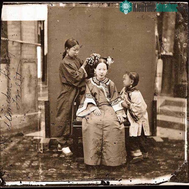 Một người phụ nữ quý tộc người Mãn đang được gia nô chỉnh sửa mái tóc.