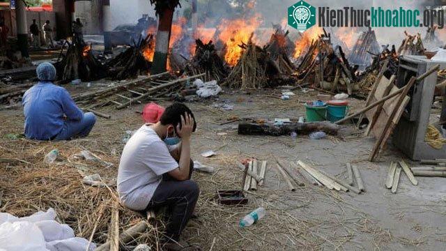 Các thành viên trong gia đình ngồi cạnh giàn hỏa táng đang cháy của những người chết vì Covid-19